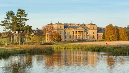 A view across the lake to the house at Croome, Worcestershire, which is surrounded by trees in autumnal shades.
